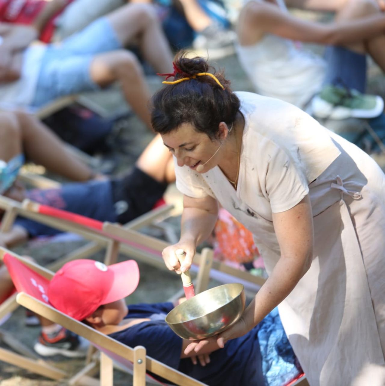 Merveilleuse-sieste-musicale Femme animant une sieste musicale en plein air avec un bol tibétain auprès d'enfants détendus