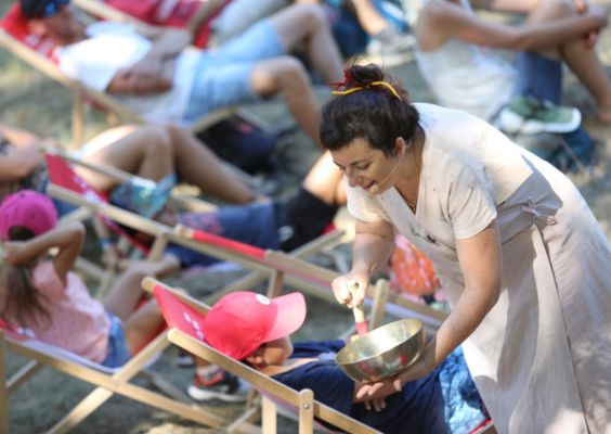 Programme Vibre & Raisonne Femme animant une sieste musicale en plein air avec un bol tibétain auprès d'enfants détendus